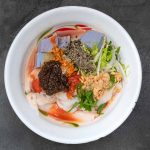 peanut and rice curd in tomato broth, topped with chilli paste, sesame, peanut, cabbage, and herbs.