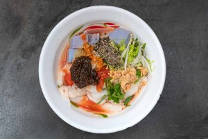 peanut and rice curd in tomato broth, topped with chilli paste, sesame, peanut, cabbage, and herbs.