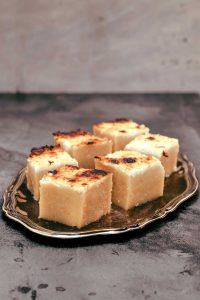 Individual squares of beige pudding cake with charred coconut cream on top
