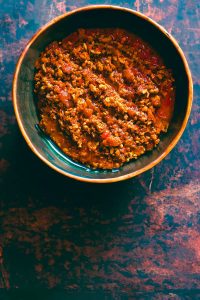 Overhead shot of a faux pork and tomato relish in a rustic bowl on a weathered metal tabletop