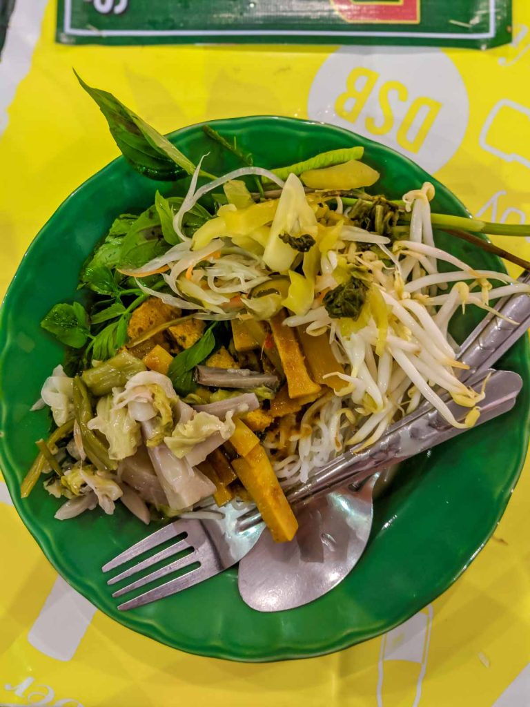 top down view of kanom jeen curry noodles loaded up with pickled mustard greens, bean sprouts, jackfruit, and herbs.