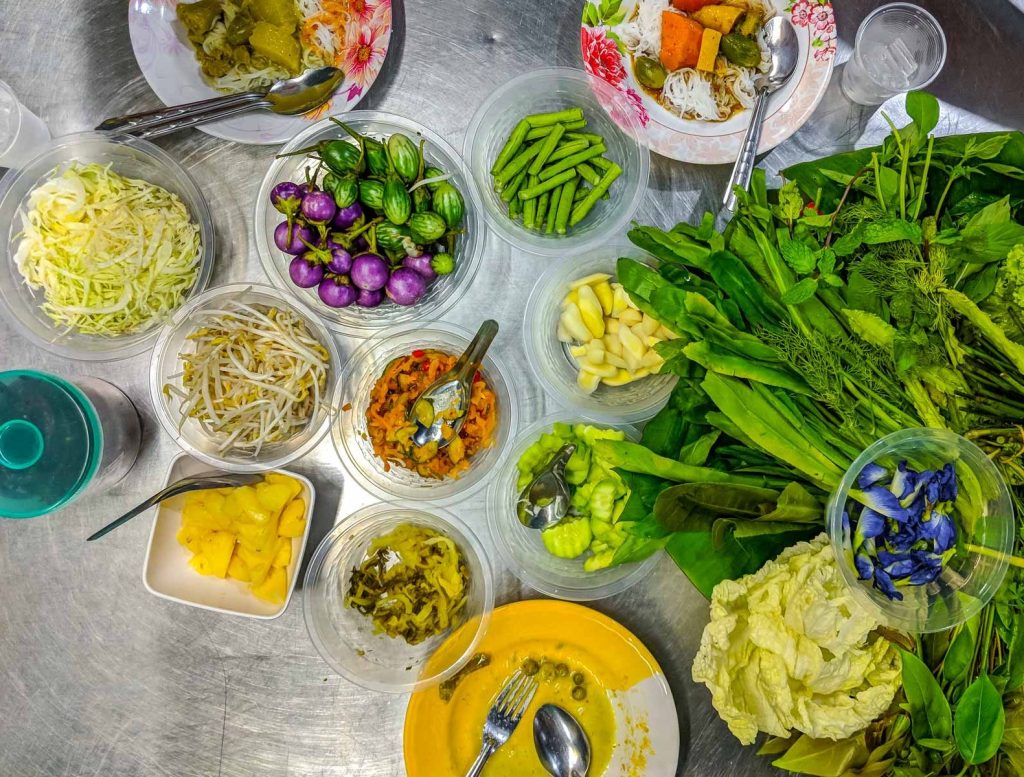Top down view of a metal table full of plastic disposable dishes full of vegetables and herbs