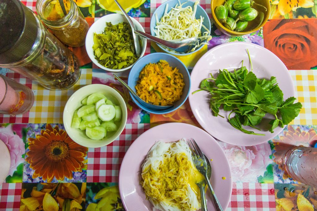 Top down view of a table packed with myriad dishes and bowls full of vegetables and curry noodles